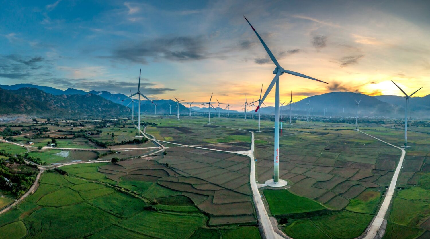 Vibrant aerial view of wind turbines in lush Vietnamese landscape at sunset, showcasing renewable energy.